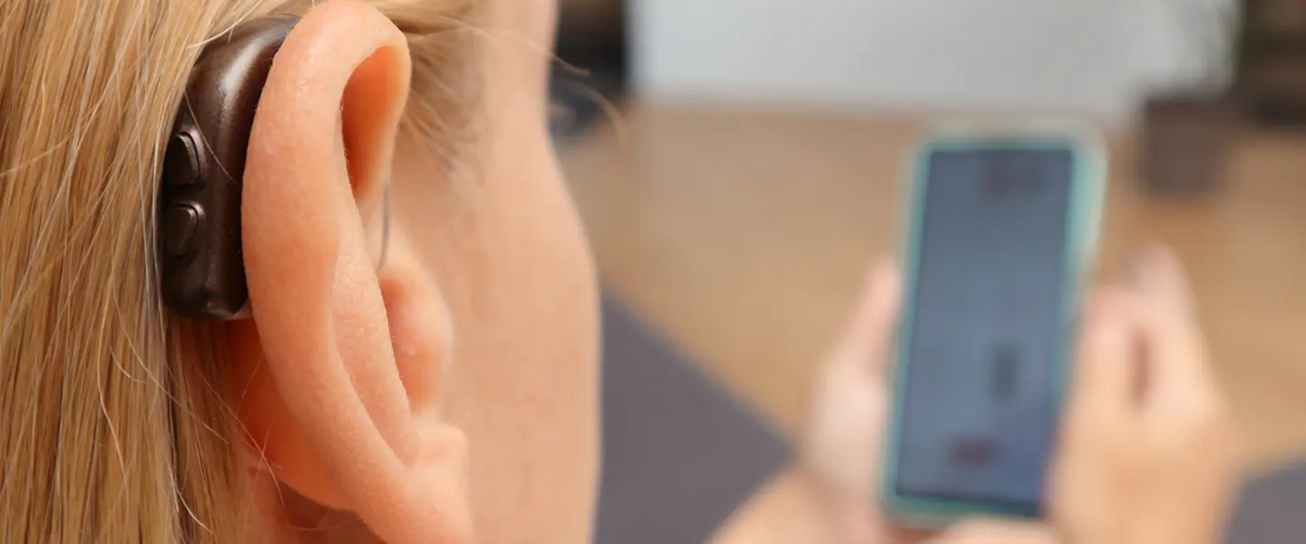 Close up of a woman wearing a hearing aid looking at her phone's hearing aid app
