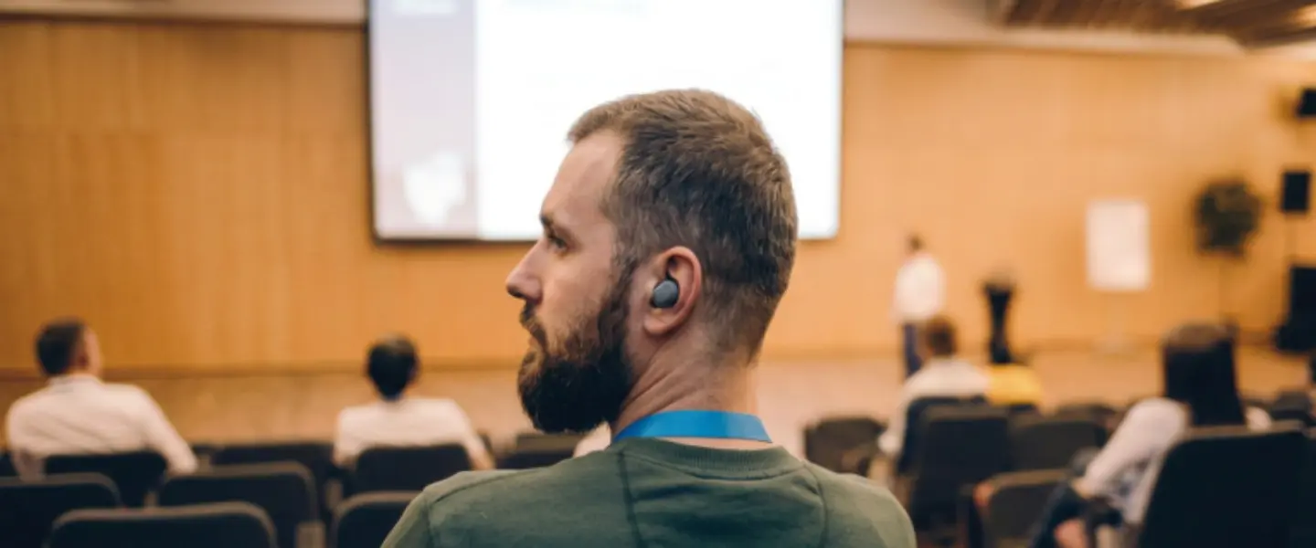 Back view of a young man wearing earbuds listening to a meeting.
