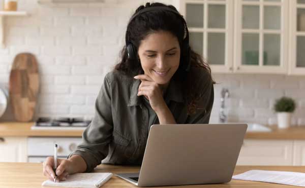 A young woman smiling while watching a webinar on her laptop.