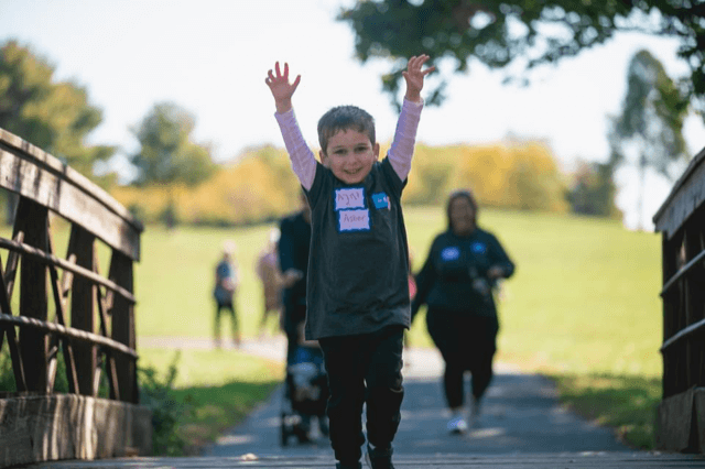 A smiling young boy raises his arms at a Walk4Hearing