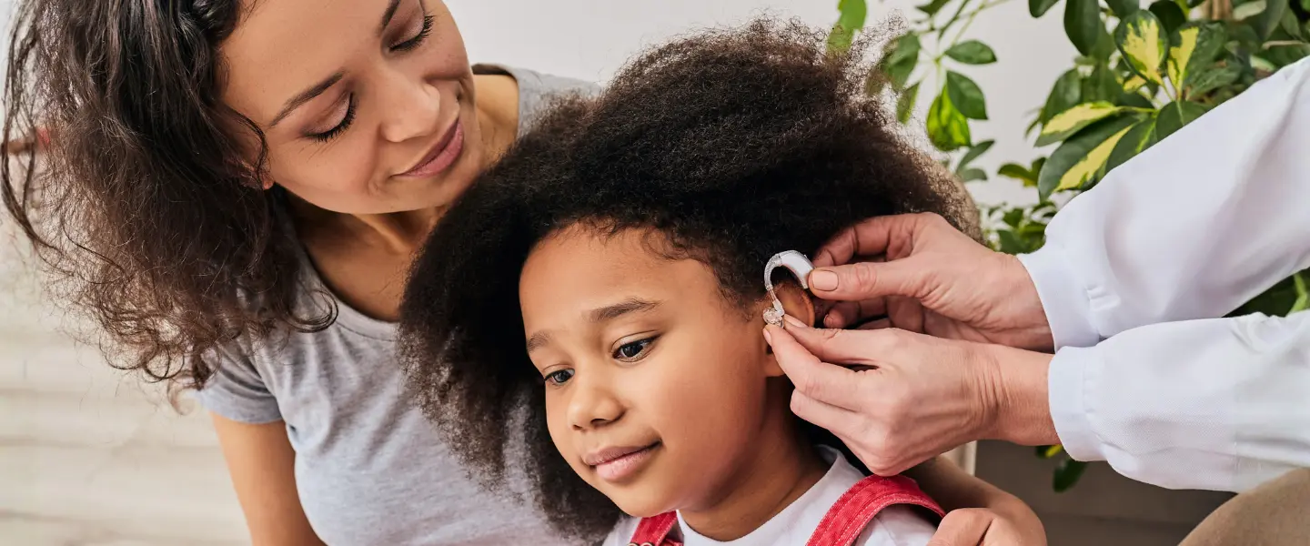 A young girl trying on a hearing aid with the support of her mother