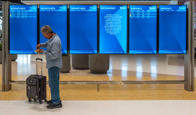 Airport visual paging and flight screens with a man in the foreground checking his phone.