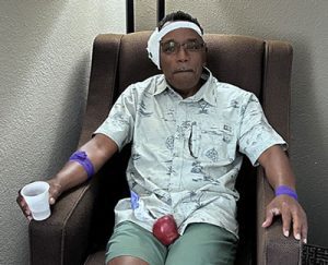 Bobby Graves seated in an armchair after his cochlear implant surgery, with a protective ear cup and bandage around his head.