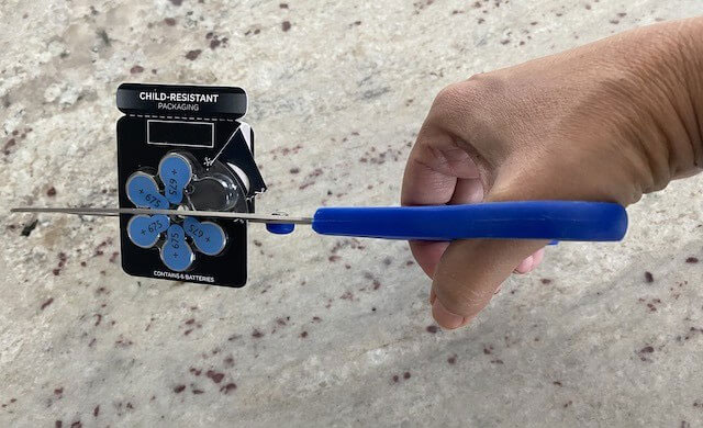Scissors cutting into a hearing aid battery package.