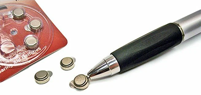 Magnetic pen pulling out a hearing aid battery from package.