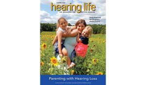 Cover of Summer 2024 issue of HLAA Hearing Life Magazine - A mom carrying 2 daughters in a field of sunflowers. "Parenting with Hearing Loss"