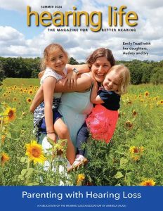 A mother carrying 2 young daughters in a field of sunflowers - Cover of Summer 2024 HLAA Hearing Life magazine issue. "Parenting with Hearing Loss"