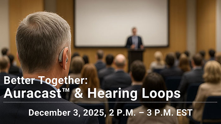 An older man wearing a hearing aid watching a presentation with the crowd in front of him in the background.